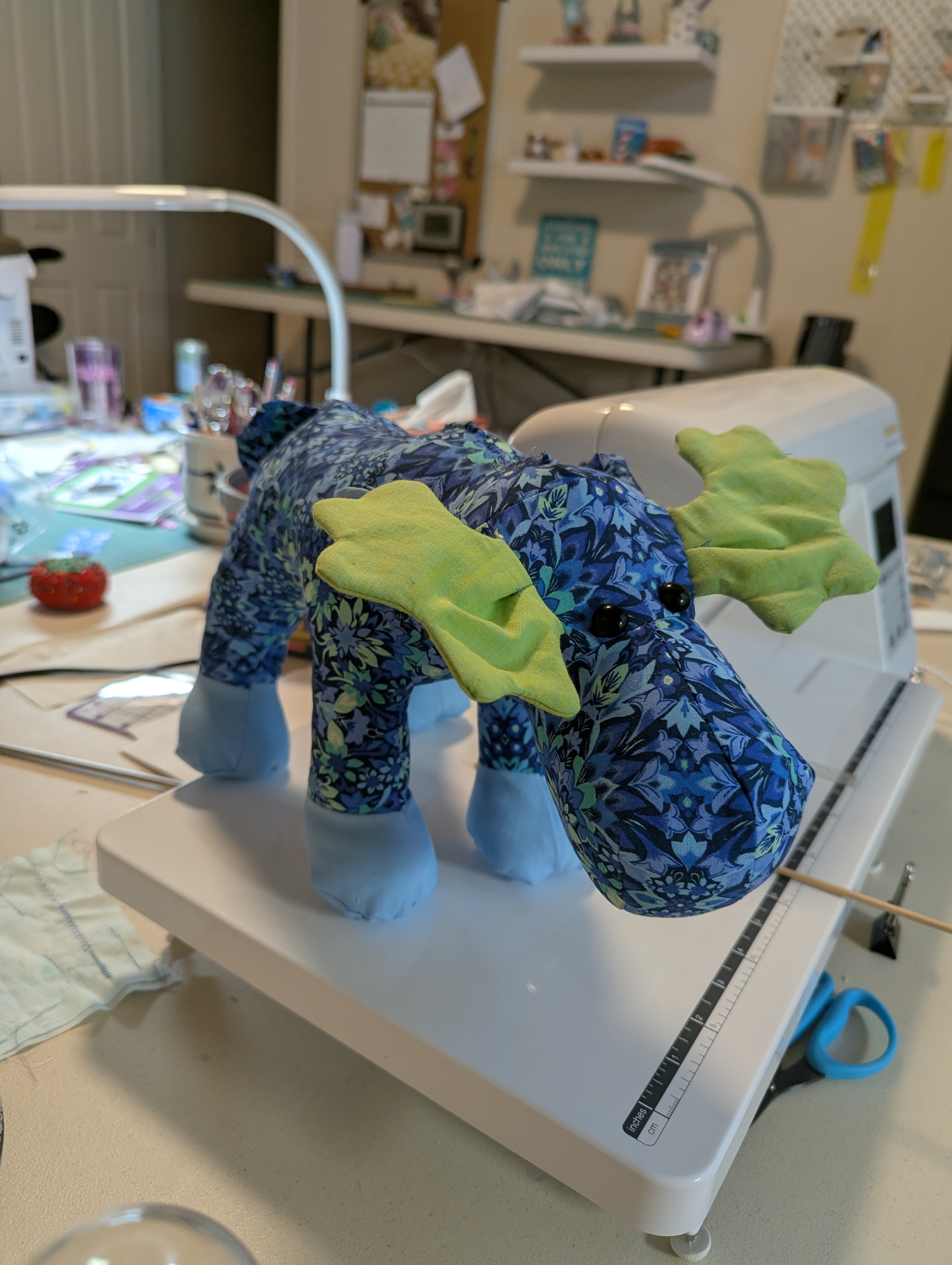 A stuffed moose sewn from blue floral fabric with green felt antlers, sitting on a sewing machine.